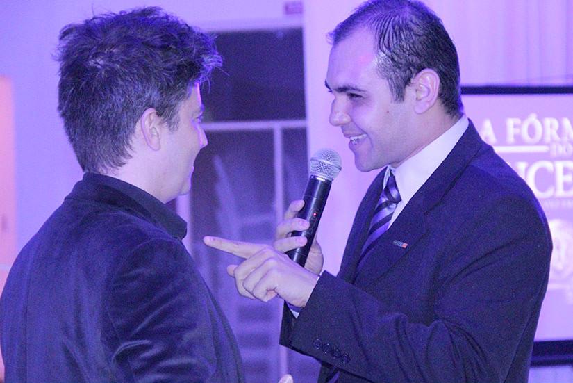 Rodney, de terno e com microfone, conversa com um convidado no palco