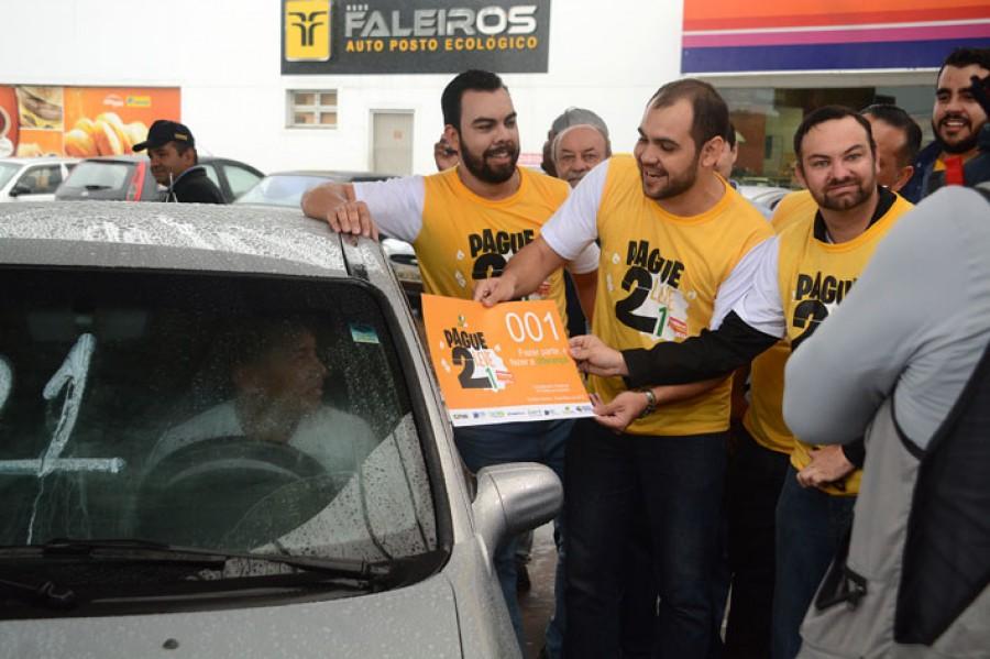 Rodney e voluntários de camiseta amarela entregam material a um motorista em um posto de combustível