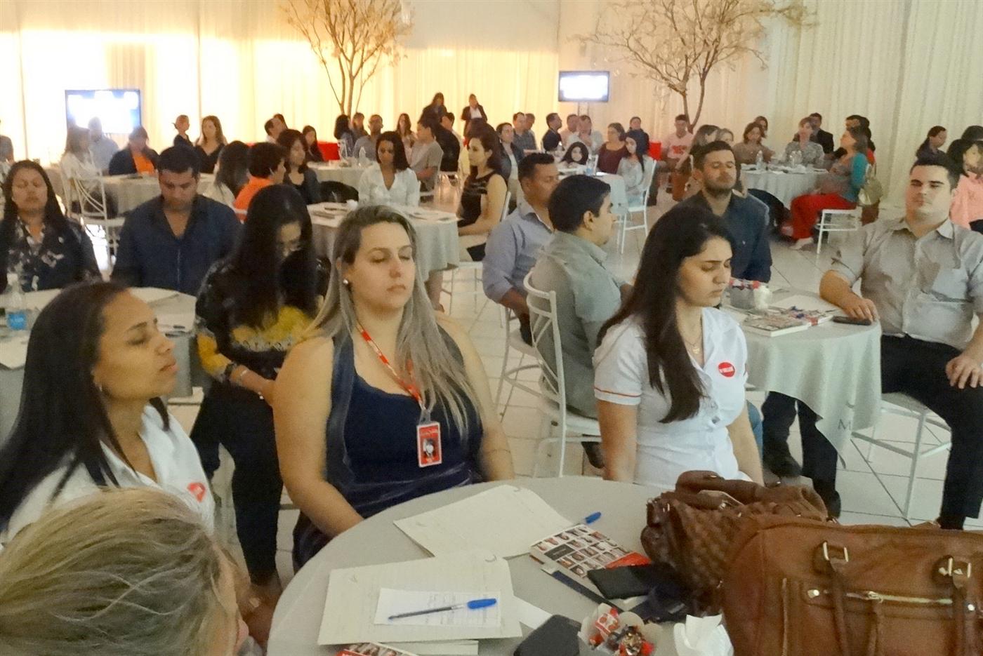 Plateia sentada em mesas redondas durante um treinamento
